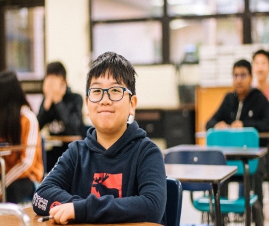 교실에 앉아 웃고 있는 안경을 쓴 어린 아이